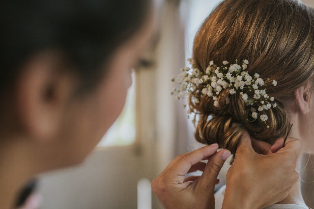 Bride's elegant updo hairstyle adorned with baby's breath flowers, styled by a hairdresser in preparation for her wedding day.
