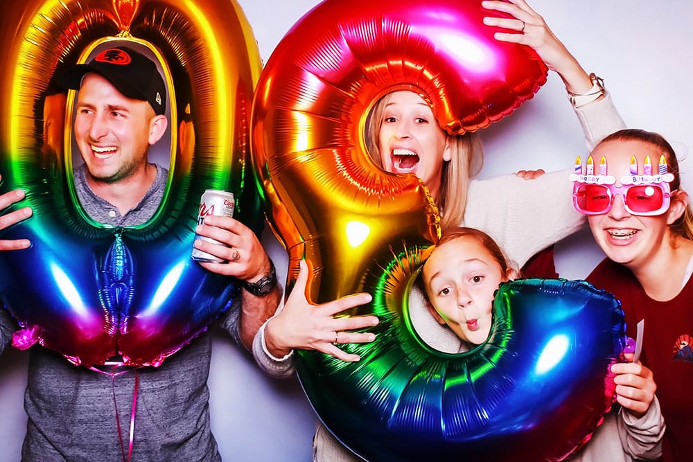 Happy family posing in a photo booth with colorful balloons, celebrating a special occasion, showcasing joyful expressions and fun accessories.