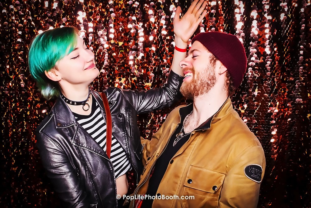 Couple enjoying playful moments in a photo booth with a sparkling backdrop, capturing joyful expressions and fun memories at a private event.