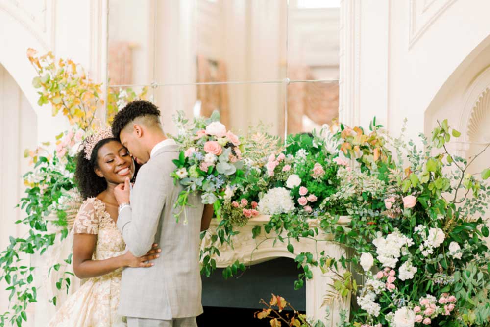 Young couple embracing in front of a floral arrangement, celebrating their wedding day, showcasing love and joy in an elegant setting.
