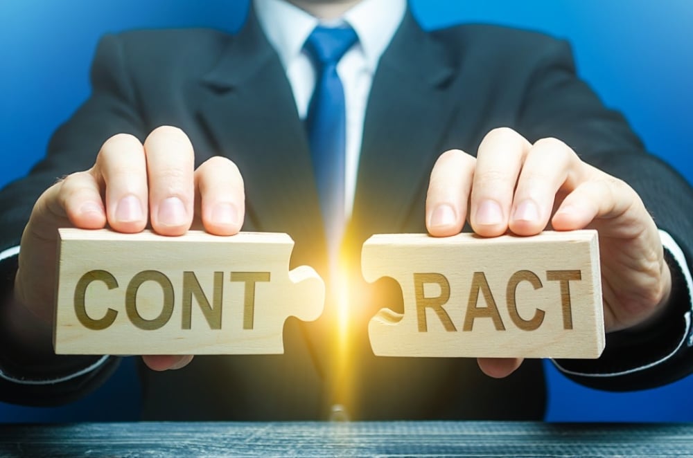 Businessman holding wooden puzzle pieces labeled "CONT" and "RACT," symbolizing contract terms and cancellation policies for event planning.