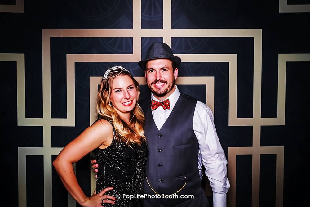 Couple posing happily in a stylish photo booth with a geometric backdrop, showcasing fun moments at a private event.