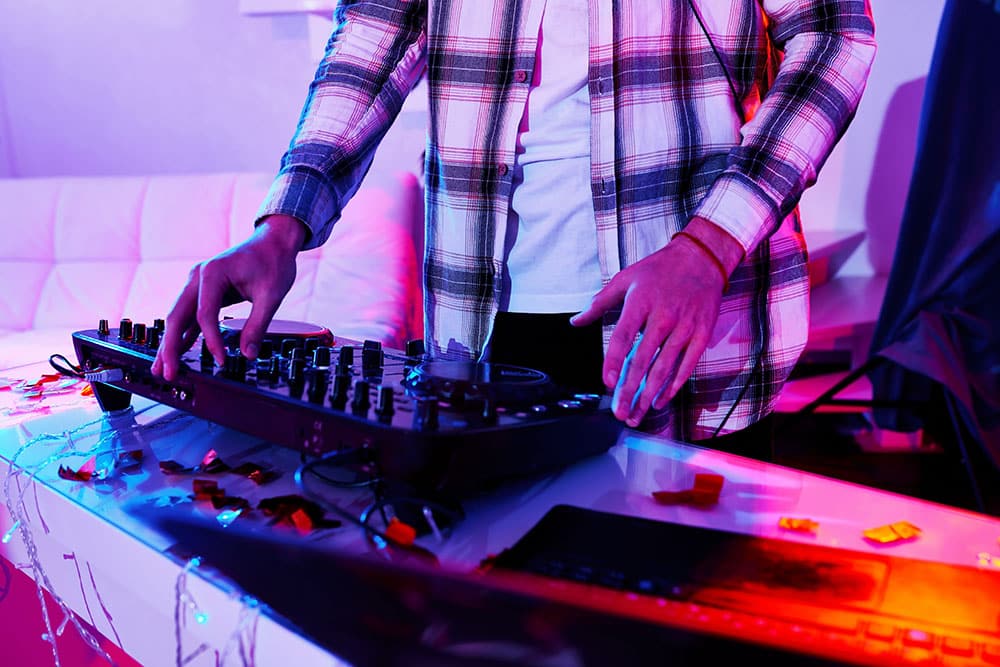 DJ mixing music on a console with colorful neon lights and confetti on the table, reflecting a vibrant party atmosphere.