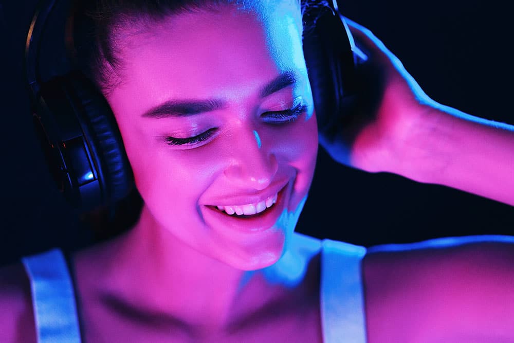 Woman enjoying music in headphones, illuminated by vibrant neon lights, representing DJ services for events.