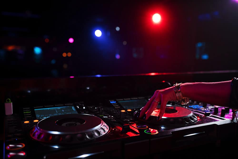 Modern DJ mixing tracks at turntables in a vibrant nightclub with colorful lighting and a smoky atmosphere.