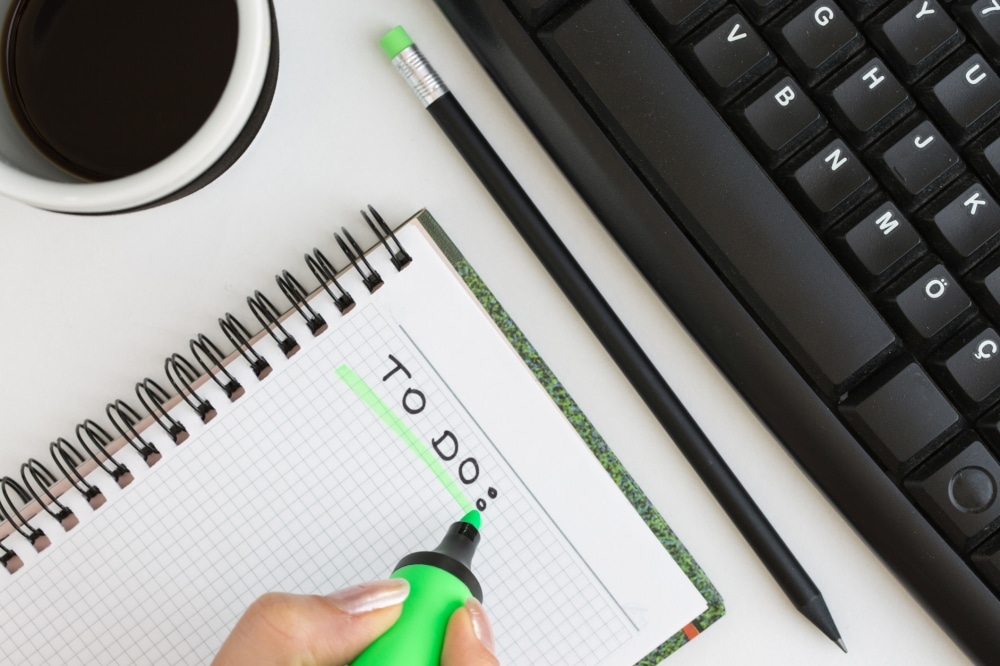 Hand highlighting "TO DO" in a notebook, with a coffee cup and keyboard in the background, symbolizing event planning and organization.