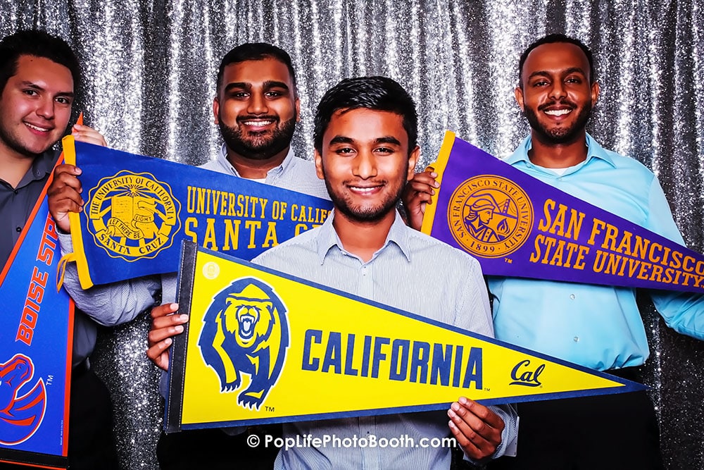Four smiling men holding university pennants in a photo booth, showcasing California universities for a corporate event.