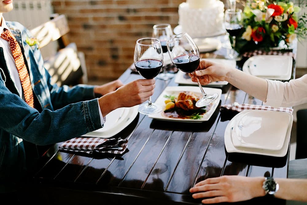Couple toasting with wine glasses at a dining table, featuring a plate of food, emphasizing networking and social interaction at a corporate event.