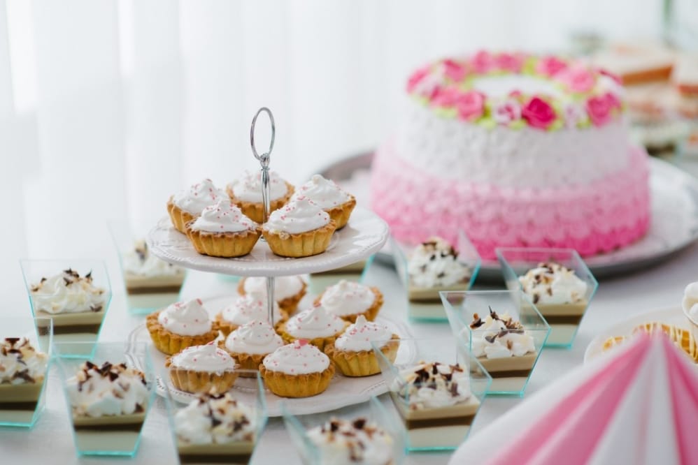 Cupcakes with whipped cream and sprinkles, layered dessert cups, and a pink wedding cake with floral decoration, ideal for entertaining kids at weddings.