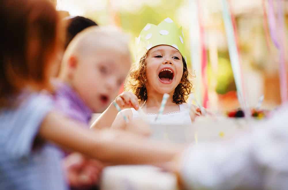 Small children enjoying outdoor wedding party activities, one girl wearing a festive crown, laughing and engaging with others at the table.