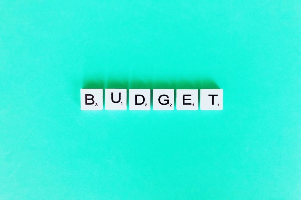 Budget spelled out in letter tiles on a turquoise background, representing financial planning challenges in wedding preparations.