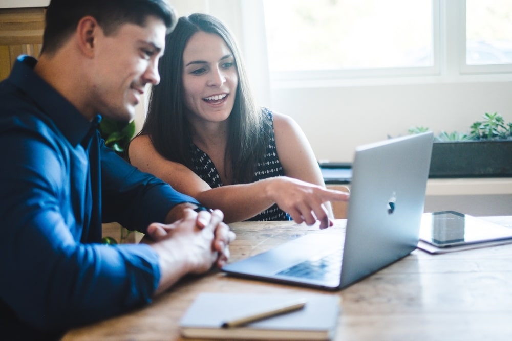 Couple discussing wedding planning details on a laptop, emphasizing collaboration and decision-making amidst wedding challenges.
