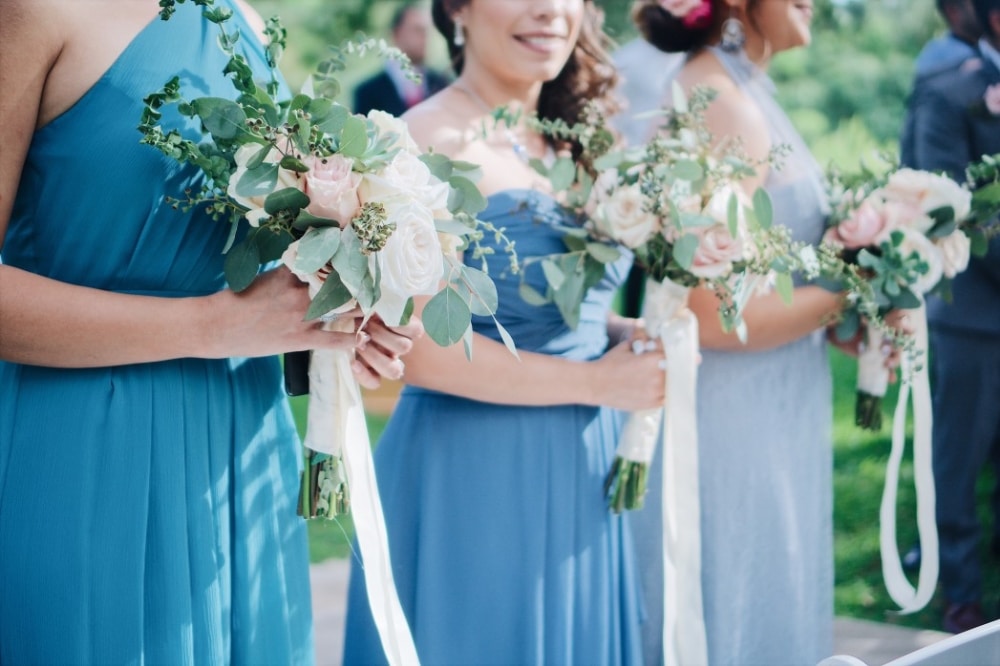 Bridesmaids in elegant powder blue dresses holding bouquets of blush roses and greenery, enhancing a romantic wedding atmosphere.