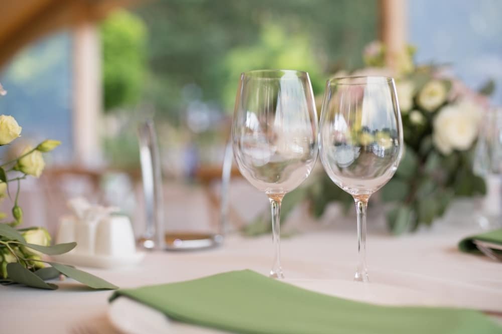 Elegant table setting with two wine glasses, green napkin, and floral arrangement, reflecting a sophisticated wedding atmosphere.