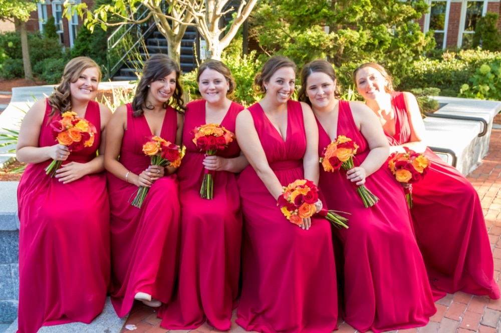 Bridesmaids in vibrant red dresses holding bouquets of orange and yellow flowers, showcasing a lively spring wedding color scheme.