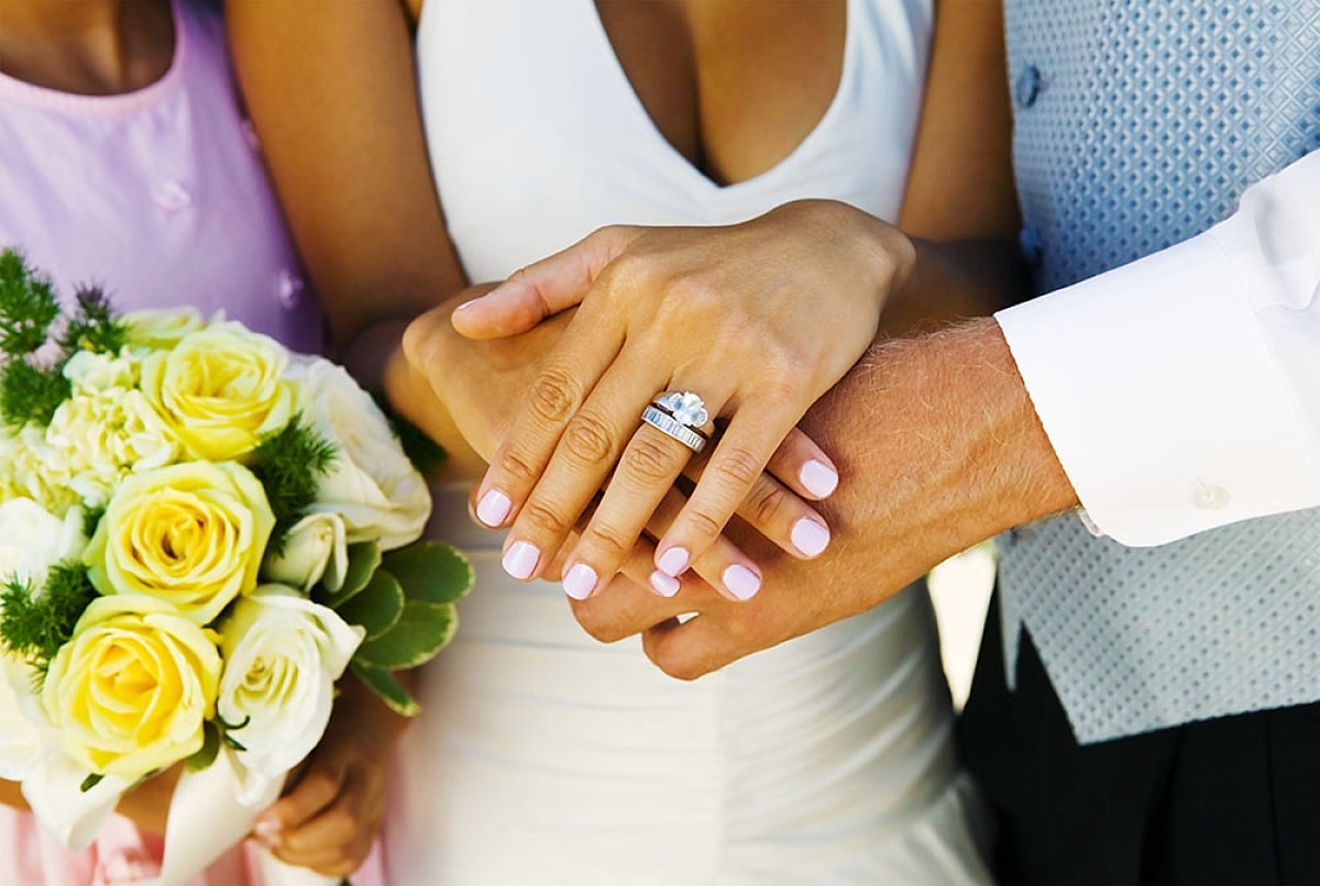 Bride and groom holding hands, showcasing a diamond wedding ring set and bouquet of yellow roses, symbolizing love and commitment in wedding planning.