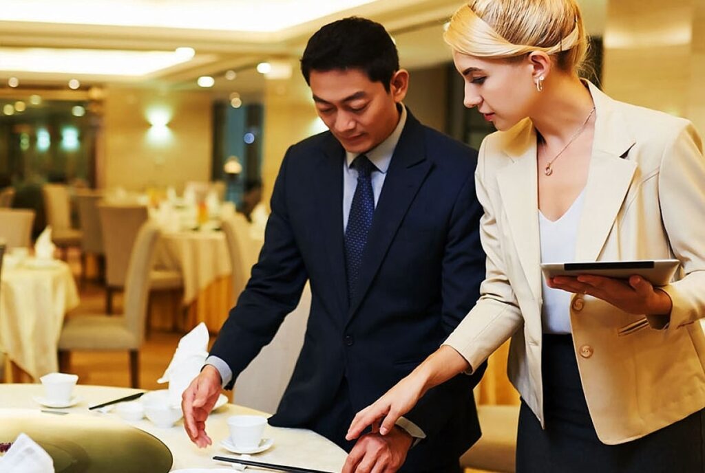 Banquet manager explaining table settings to waiter in elegant restaurant setting, emphasizing event planning and coordination.