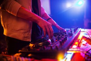 Close-up of DJ's hands mixing tracks on a turntable with colorful lights in a trendy club, enhancing event atmosphere and enjoyment.