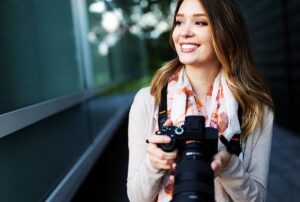 Woman smiling while holding a DSLR camera, showcasing professional photography skills, relevant to event planning and capturing memorable moments at celebrations.