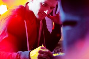 Young DJ mixing music at a vibrant event, focused on turntables with colorful lights in the background, enhancing the party atmosphere.