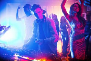 DJ performing at vibrant party with colorful lights, surrounded by energetic crowd dancing and enjoying the music.