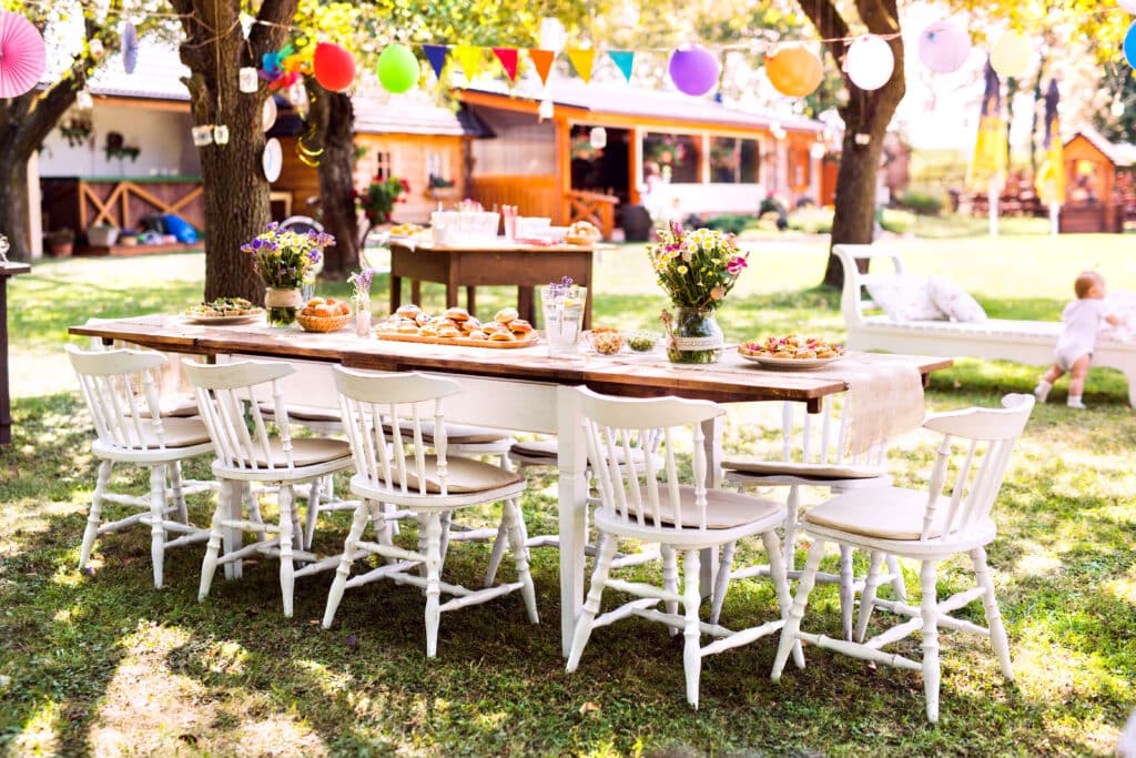Outdoor corporate event setup with a long farmhouse table, white chairs, and fresh floral centerpieces at a garden celebration in the Bay Area.
