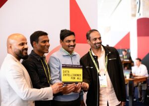 Four attendees at the Databricks event holding a sign that reads "DATA INTELLIGENCE FOR ALL," showcasing engagement and networking in a vibrant booth setting.