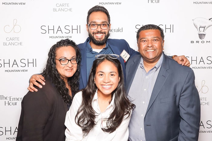 Group of four smiling individuals posing in front of a branded backdrop for the grand opening of Shashi Hotel in Mountain View, showcasing a celebratory atmosphere and the hotel's modern aesthetic.
