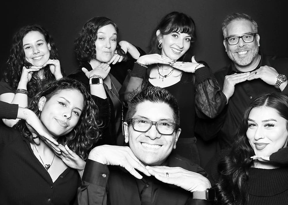 Group of six people posing playfully in a photo booth, showcasing fun expressions and hand gestures, ideal for graduation celebration memories.