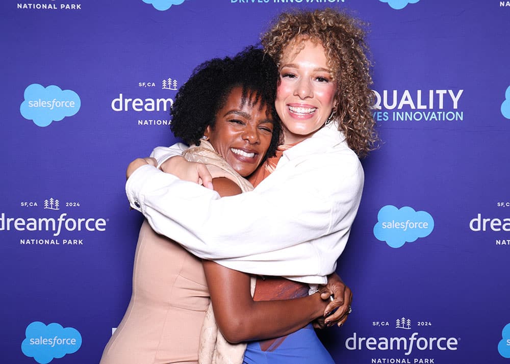Two women hugging joyfully in front of a colorful backdrop featuring "dreamforce" and "salesforce" logos, capturing a heartfelt moment perfect for photo booth memories.