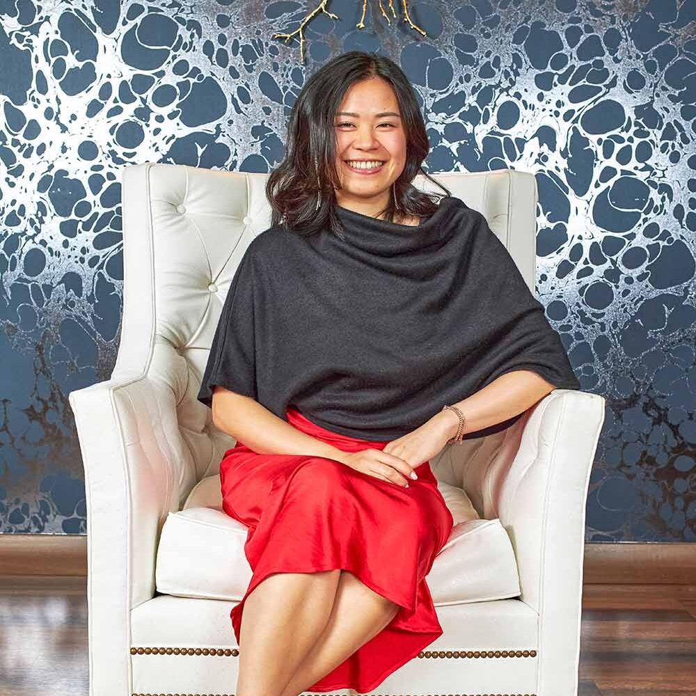 Woman in elegant attire seated in a plush white chair, smiling against a stylish backdrop, showcasing the luxurious ambiance of Hotel Nikko, ideal for events like the BAMIES Awards Gala.