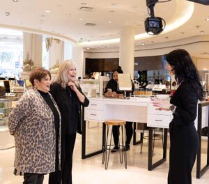 Two women engaging with a presenter in a modern retail space, showcasing a branded photo booth experience with professional lighting and interactive elements for corporate events.