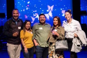 Group of five people posing together at a vibrant event, with a colorful backdrop featuring abstract designs, illustrating social engagement at a photo booth event for marketing and brand interaction.