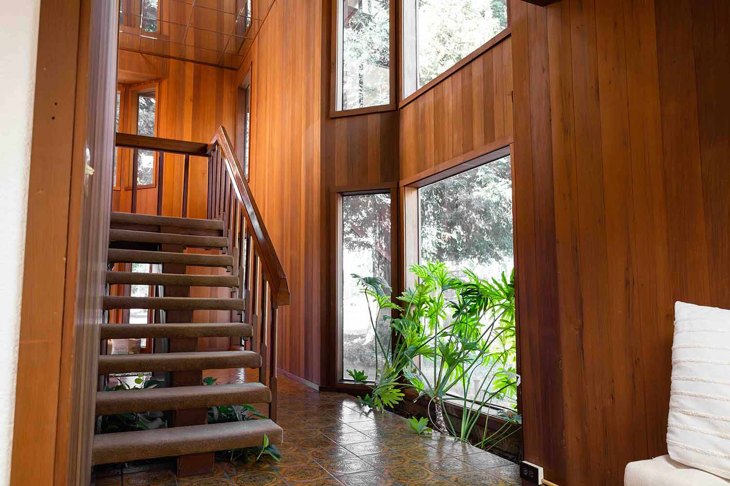 Wood-paneled staircase leading to upper level, surrounded by large windows and indoor plants, reflecting RMC's commitment to authenticity and connection in their new Healdsburg office.