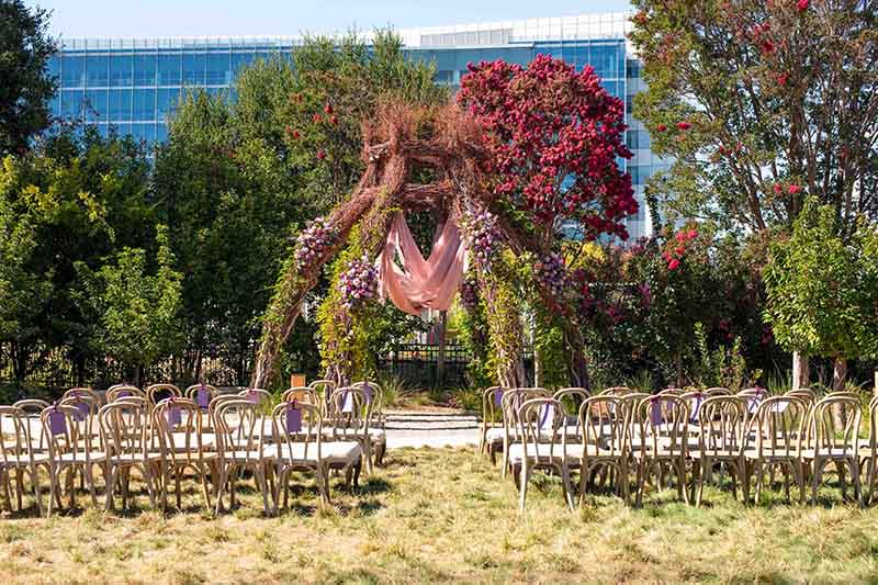Outdoor wedding ceremony setup at Treehouse Hotel featuring floral arch and rows of chairs, surrounded by greenery and modern buildings, ideal for eco-conscious couples.