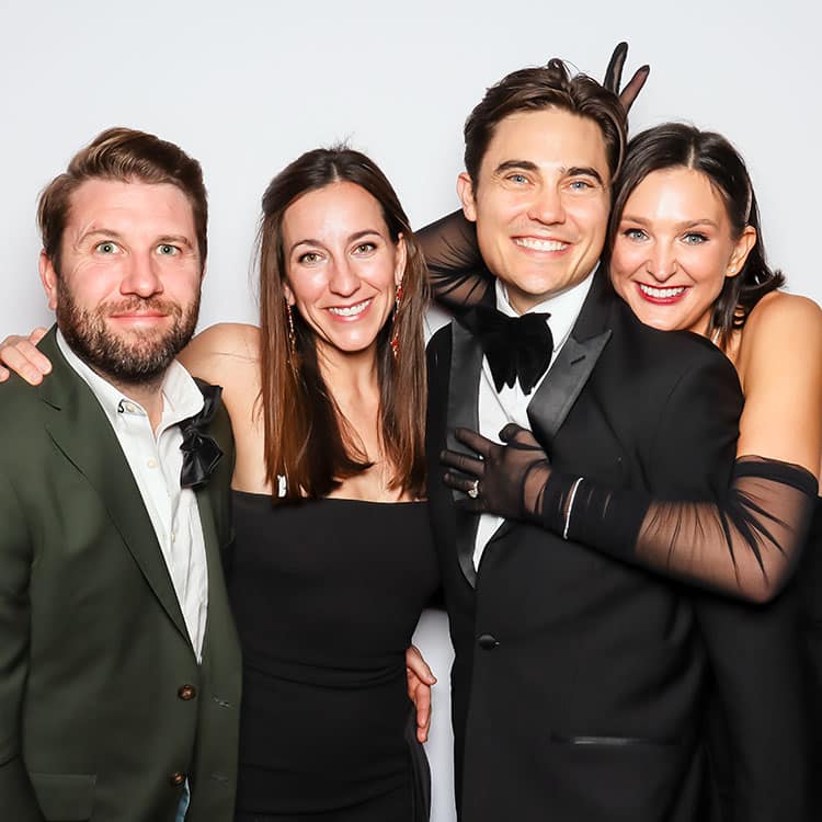 Group of four elegantly dressed guests posing together in a photo booth, showcasing Hollywood glamour with stylish attire and joyful expressions.