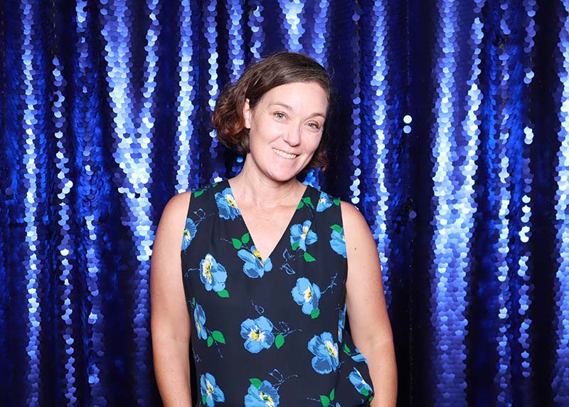 Woman smiling in front of a shimmering cobalt blue sequin backdrop, showcasing a glamorous photo booth setting ideal for upscale events and celebrations.