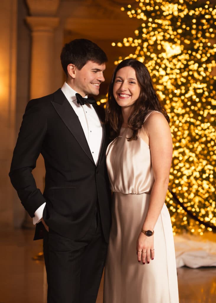 Couple smiling in formal wear against a holiday portrait studio backdrop.