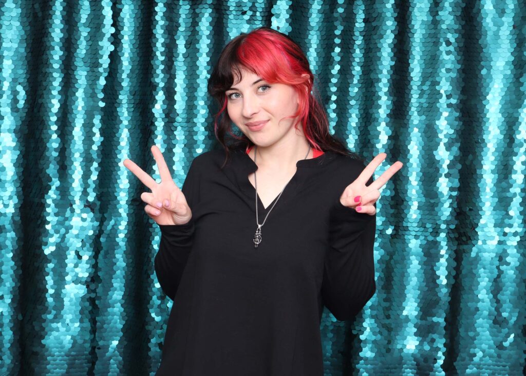 Person posing with peace signs in front of shimmering blue sequin backdrop, ideal for glamorous photo settings and upscale events.