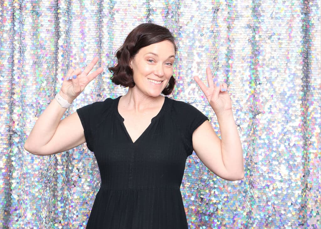 Woman posing with peace signs in front of a shimmering holographic sequin backdrop, ideal for upscale events and photo booths.