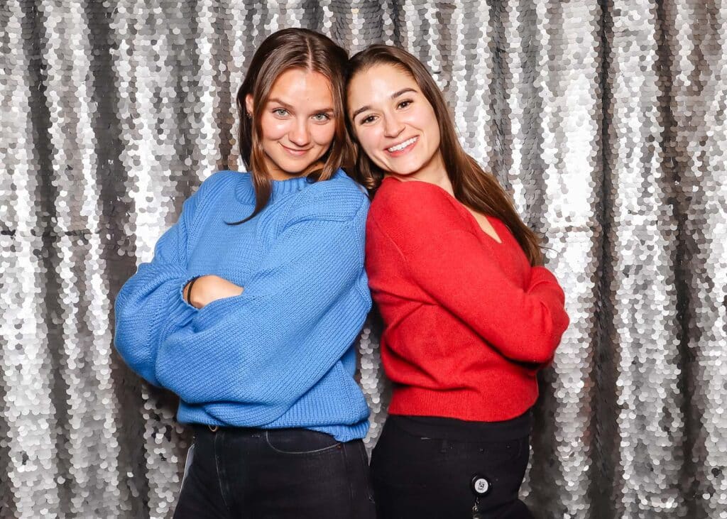 Two women posing back-to-back in front of a shimmering silver sequin backdrop, showcasing a glamorous photo setting ideal for upscale events and celebrations.