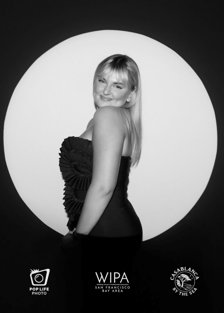 Woman posing in elegant black dress with ruffled details, dramatic lighting highlighting her features against a circular backdrop, showcasing high-contrast black-and-white photography style of Spotlight Photo Booth by Pop Life Photo.