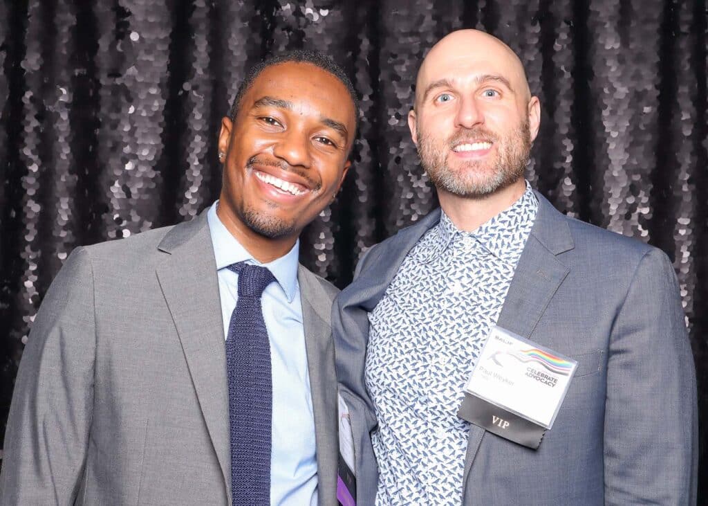 Two smiling men posing together in front of a shimmering black sequin backdrop, ideal for upscale photo booth settings.