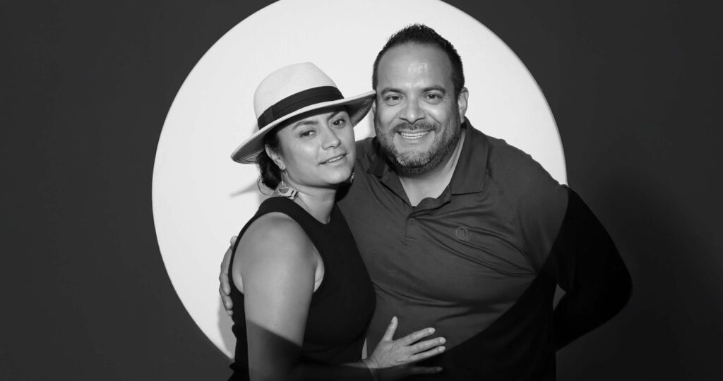 Couple posing together in a stylish black and white portrait with a circular light backdrop, showcasing high-energy, immersive photo experience at an event.