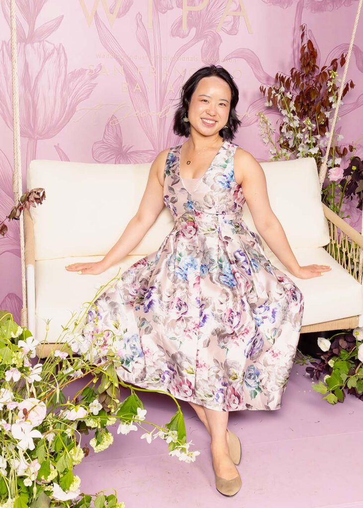 Woman in floral dress sitting on a swing in a styled studio environment with floral decorations, showcasing a personalized portrait experience.