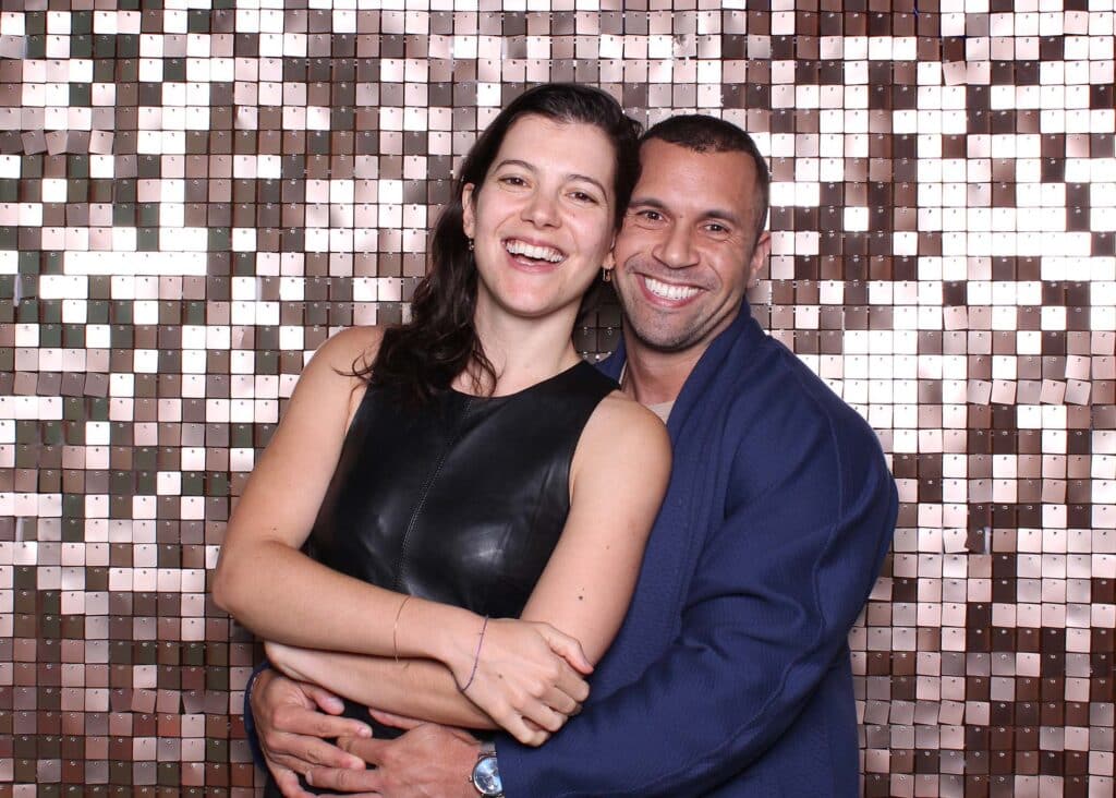Couple smiling and embracing in front of a champagne sequin shimmer wall, ideal for modern luxury events and photo booth backdrops.