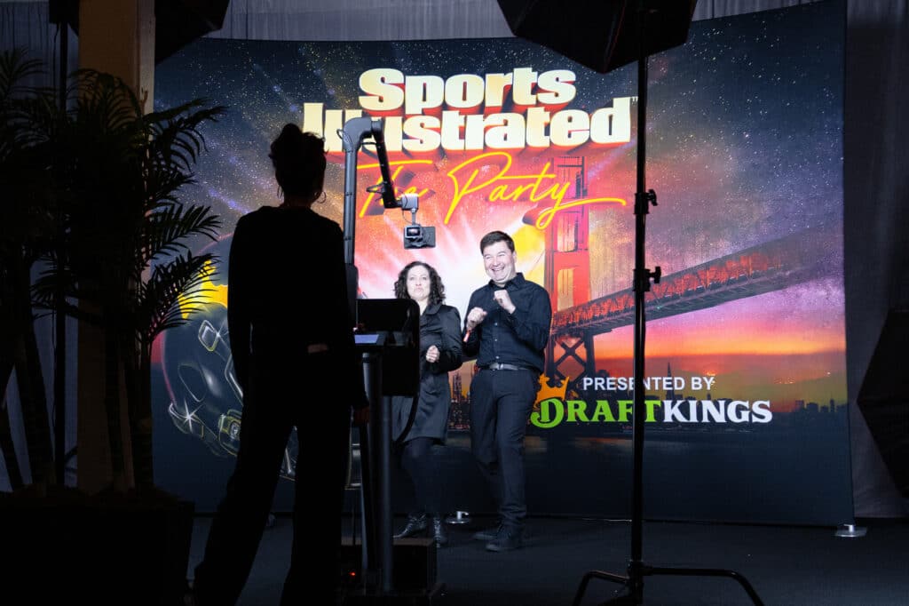 Photo booth setup at a Sports Illustrated party featuring a vibrant backdrop with the Golden Gate Bridge, illuminated by colorful lighting, capturing guests in a festive atmosphere.