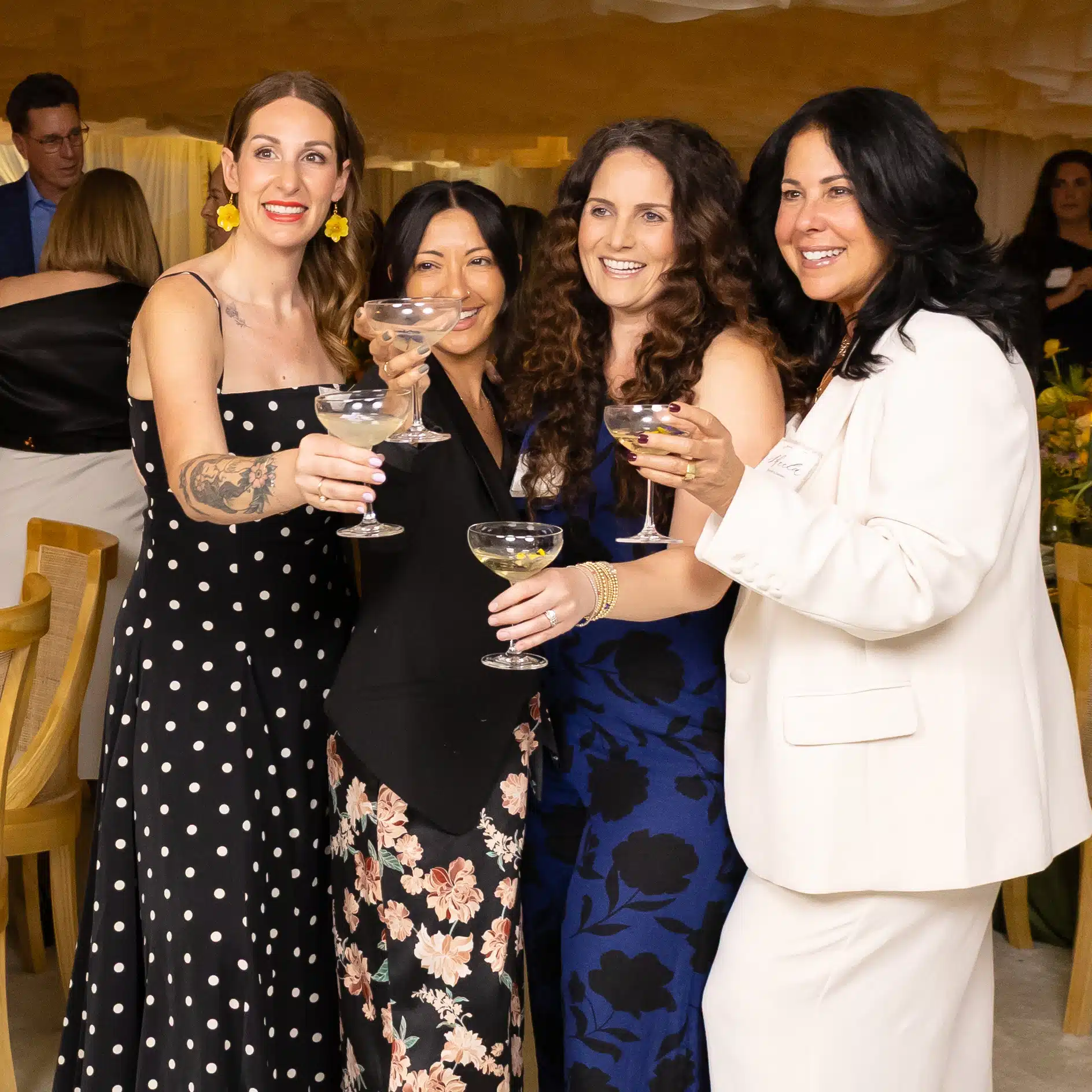 Group of four women celebrating with cocktails at a corporate event, showcasing vibrant attire and joyful expressions, emphasizing engagement and social interaction.