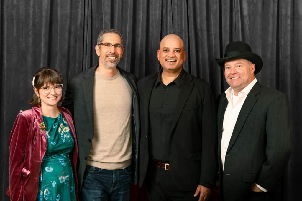 Group of four individuals posing in front of a gray velvet backdrop, showcasing a sophisticated setting ideal for upscale events and formal portraits.