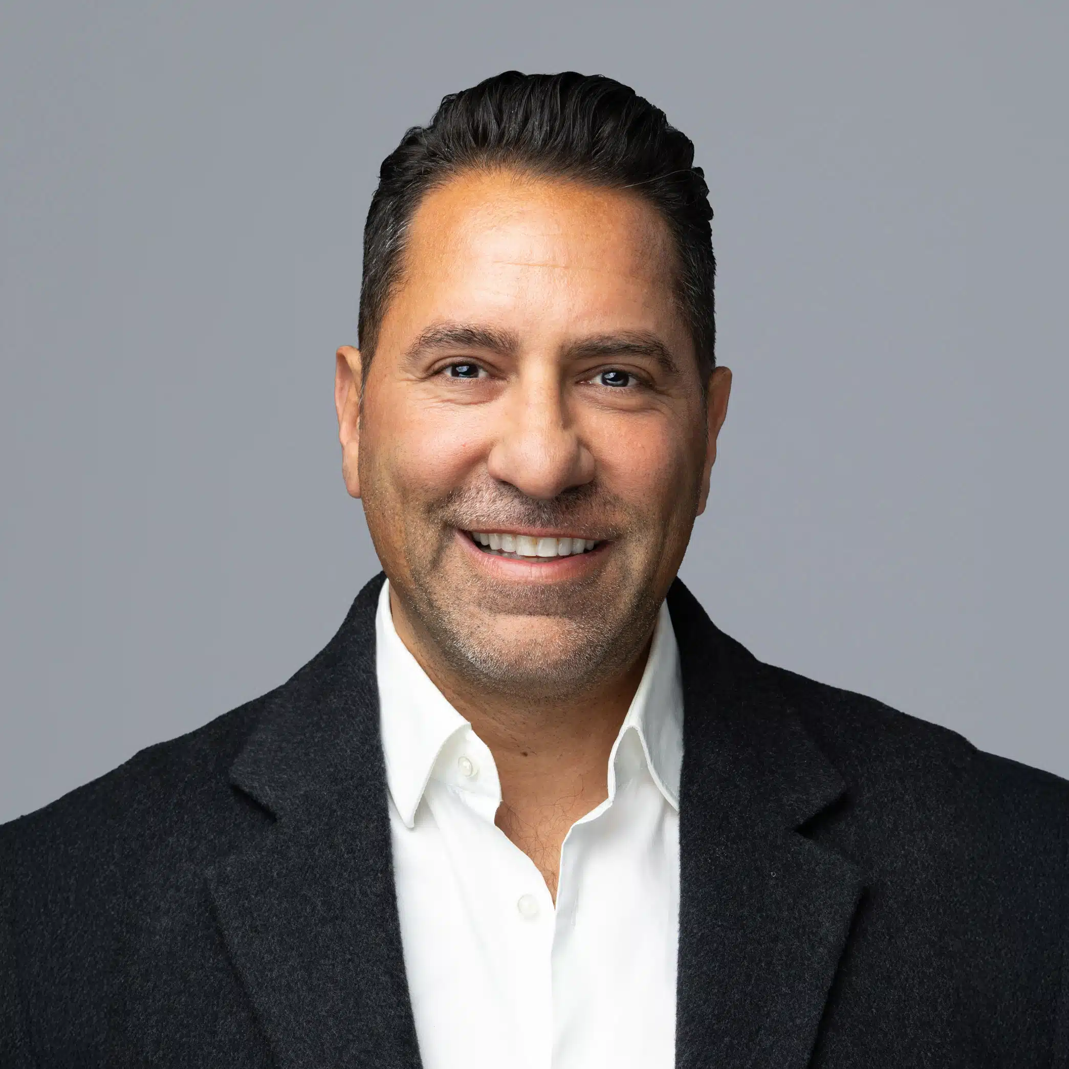 Professional headshot of a smiling man in a black blazer and white shirt against a neutral gray background, showcasing polished photography for corporate events and branding.